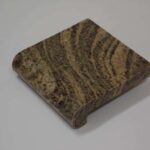 Square granite stone sample tile with tan, brown, and dark grey wavy veining and a rounded bullnose front edge.