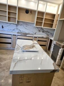 High-angle view of a secondary kitchen island with marble countertop during installation, featuring open upper cabinetry and matching backsplashes.