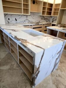 High-angle view of a modern unfinished kitchen with a dramatic marble waterfall island and matching marble backsplashes.