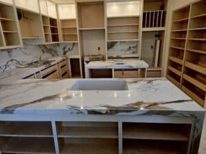 High-angle view of an unfinished modern kitchen featuring white marble islands, full-height backsplash, and extensive custom wood cabinetry.
