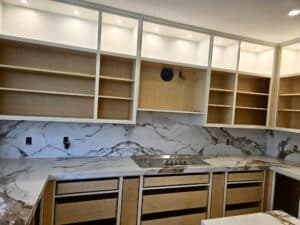 Unfinished modern kitchen with installed marble countertops, marble backsplash, and open upper and lower cabinetry frames.