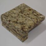A small square sample block of tan and brown speckled granite featuring an ogee-style finished edge.