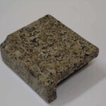 A small square sample block of dark brown and black speckled granite with a bevel edge profile.