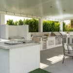 Covered outdoor patio featuring a spacious kitchen with white stucco cabinetry, marble countertops, built-in stainless steel grills, and woven lounge seating.