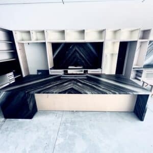 Modern kitchen under construction featuring custom book-matched dark marble island and backsplash surrounding white cabinetry frames.