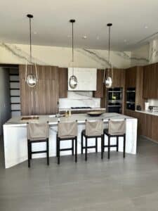 Modern luxury kitchen featuring a marble waterfall island with four barstools and three brass pendant lights.