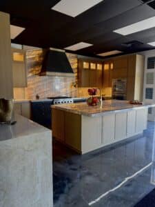 Kitchen showroom display featuring backlit quartzite countertops and backsplash, light oak cabinetry, dark range hood, and a large central island.