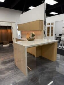 Modern kitchen showroom display featuring a light oak island with a waterfall white marble countertop, matching upper cabinets, and glossy metallic floor.