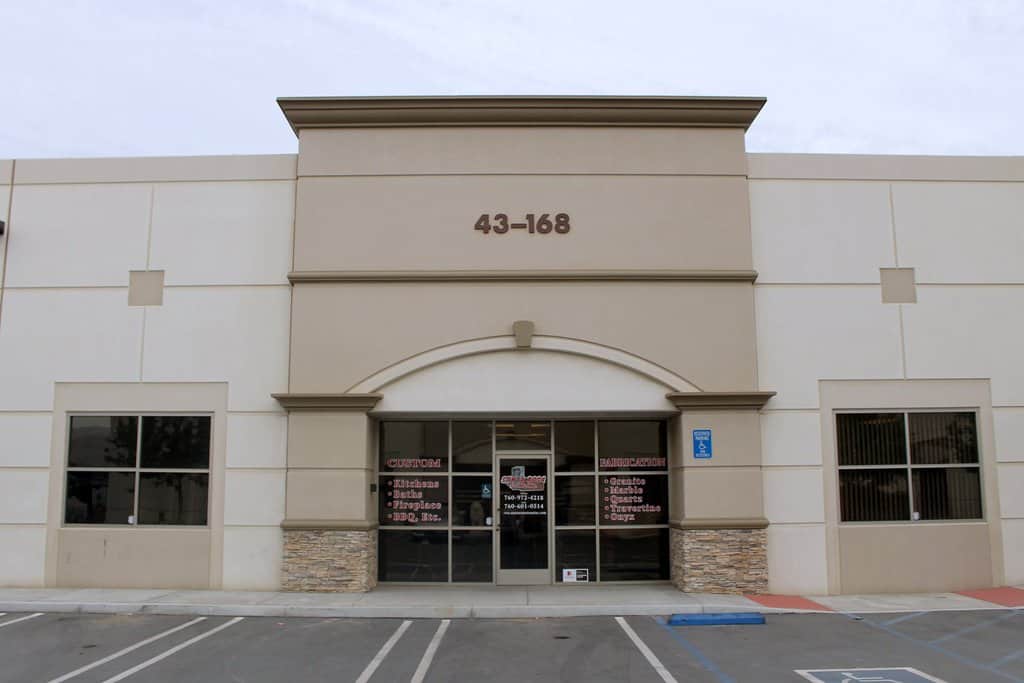 Exterior storefront of a custom stone fabrication business with the address number 43-168 displayed above a glass entryway.