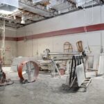 Industrial stone fabrication shop floor with bridge saw machinery, transport carts, and large ventilation fans.