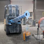 Forklift equipped with a blue boom attachment and stone slab lifting clamp inside an industrial warehouse.