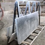 Cut stone countertop slabs leaning on a metal A-frame transport cart in a fabrication workshop.