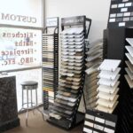 Showroom interior displaying several vertical racks filled with stone and quartz countertop sample slabs near a glass storefront window.