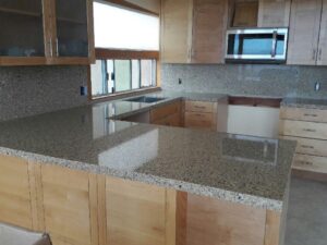 Polished gray and black speckled granite countertops and matching full-height backsplash in a kitchen with light wood cabinetry.