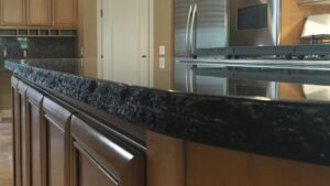 Close-up profile of a black granite kitchen island featuring a chiseled, rock-face edge on warm wooden cabinets.