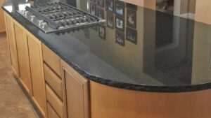 A polished black granite kitchen island with a built-in gas cooktop set atop light wood cabinets.