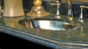 Polished dark green granite vanity countertop featuring a stainless steel undermount sink, a chrome faucet, and a decorative double-beveled edge profile.
