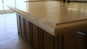 Close-up of a smooth beige stone countertop with a custom rounded step-edge profile on dark wood kitchen cabinets.