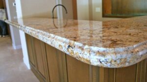Close-up of a polished beige and brown granite island countertop featuring a decorative rounded edge profile and a dark gooseneck faucet.