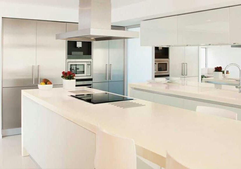Ultra-modern white kitchen featuring a large island with cooktop, stainless steel ventilation hood, and integrated stainless steel appliances.
